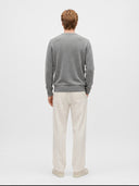 A man viewed from behind wearing a heather gray long-sleeve crewneck sweater and off-white trousers, standing against a light gray studio background.