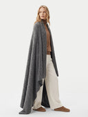 A woman modeling a long, open-front cable-knit cardigan in dark gray, worn over a brown top and cream wide-leg trousers, against a plain light gray studio background.