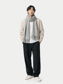 Man wearing a beige sweater, white shirt, black pants, and gray scarf on a white background