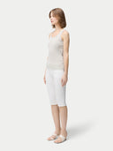 A woman wearing a beige lightweight cashmere silk tank top with no visible pattern or print, paired with white trousers. #color_pure-white