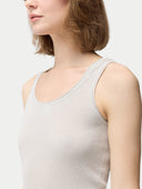 A woman wearing a beige lightweight cashmere silk tank top with no visible pattern or print, paired with white trousers. #color_pure-white