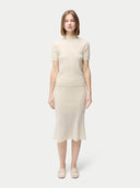 A woman wearing a beige high neck, short-sleeve cashmere top paired with a matching skirt. #color_off-white