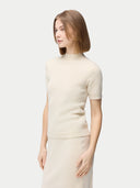 A woman wearing a beige high neck, short-sleeve cashmere top paired with a matching skirt. #color_off-white