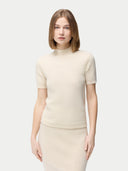 A woman wearing a beige high neck, short-sleeve cashmere top paired with a matching skirt. #color_off-white