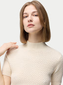 A woman wearing a beige high neck, short-sleeve cashmere top paired with a matching skirt. #color_off-white