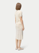 A woman wearing a beige high neck, short-sleeve cashmere top paired with a matching skirt. #color_off-white
