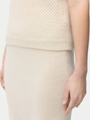 A woman wearing a beige high neck, short-sleeve cashmere top paired with a matching skirt. #color_off-white