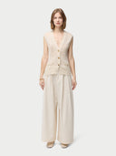 A woman wearing a beige sleeveless cashmere vest with a round neckline and button closures, paired with a white skirt. #color_off-white