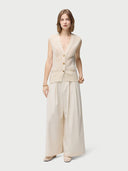 A woman wearing a beige sleeveless cashmere vest with a round neckline and button closures, paired with a white skirt. #color_off-white