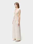 A woman wearing a beige sleeveless cashmere vest with a round neckline and button closures, paired with a white skirt. #color_off-white