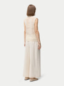 A woman wearing a beige sleeveless cashmere vest with a round neckline and button closures, paired with a white skirt. #color_off-white