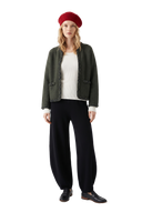 Woman in a dark green hand-braided cashmere cardigan jacket over a white ribbed top, black barrel-leg knit trousers, a red knit beret and black loafers