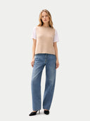 front view of a woman wearing a beige sleeveless sweater and blue jeans on a white background
