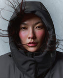 A woman in a black CashmereTech hood against a pale wall