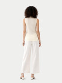 Woman wearing a cream sleeveless top and white pants on a light gray background #color_cream-white