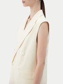 Woman wearing a white sleeveless cashmere blazer on a plain background #color_off-white