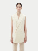 Woman wearing a white sleeveless cashmere blazer on a plain background #color_off-white