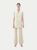 Woman wearing a white sleeveless cashmere blazer on a plain background #color_off-white