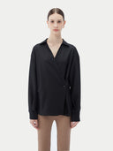 A woman wearing a black cashmere wrap shirt with a V-neck and single-button closure. #color_black