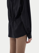 A woman wearing a black cashmere wrap shirt with a V-neck and single-button closure. #color_black