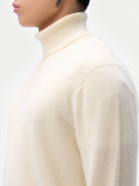 Cream turtleneck cashmere  sweater worn by a person on a plain background. #color_off-white