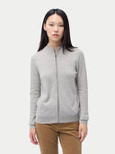 A woman standing and facing the camera, wearing a full-zip cardigan in a light color with side pockets, paired with brown trousers. #color_steel-silver