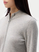 A woman standing and facing the camera, wearing a full-zip cardigan in a light color with side pockets, paired with brown trousers. #color_steel-silver
