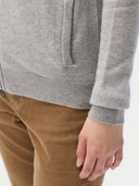 A woman standing and facing the camera, wearing a full-zip cardigan in a light color with side pockets, paired with brown trousers. #color_steel-silver
