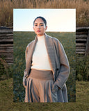 Woman in a grey cashmere coat with a knitted shawl collar over a cream turtleneck and pleated trousers