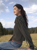 Woman in a dark green cable-knit cashmere jumper sitting on a wooden fence