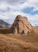 Granite rock formation on autumn grassland with snow-capped mountains behind