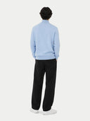 Person wearing a light blue cashmere sweater, black pants, and white shoes on a white background #color_muted-blue