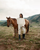 A woman in a white cashmere sweater and trousers standing beside a horse on the Mongolian steppe