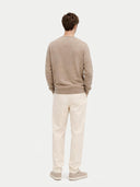 A man wearing a light brown knit V-neck cashmere cardigan over a white t-shirt, photographed against a solid light gray background. #color_taupe