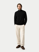 Man wearing a black sweater, beige pants, and brown shoes on a white background