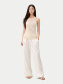 Woman wearing a beige sleeveless cashmere top and white pants on a white background. #color_off-white