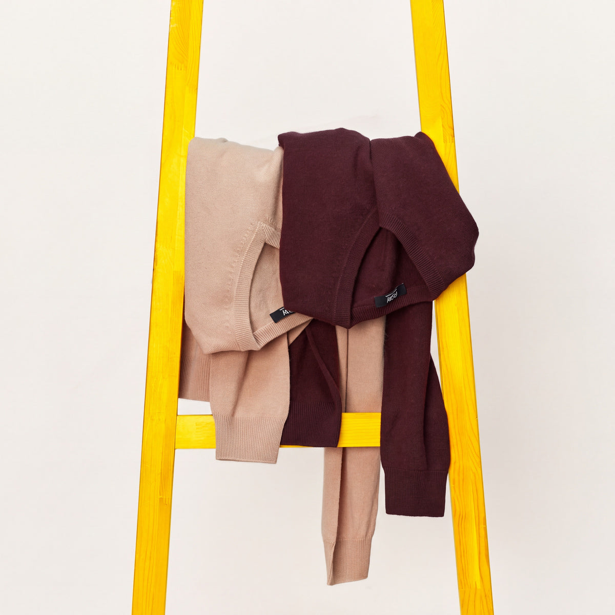 Camel and burgundy cashmere sweaters draped over a yellow wooden ladder