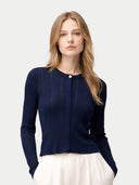 A woman modeling a navy blue ribbed knit cardigan with a single button closure, paired with white trousers, against a light gray studio background.#color_dark-indigo