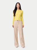 A woman modeling a bright yellow long-sleeve knit top with a front zipper, paired with beige wide-leg trousers, against a light gray studio background. color_vivid-yellow #ai-image
