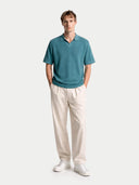Man wearing a teal polo shirt and beige pants on a white background.