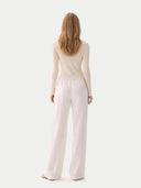 Woman wearing a beige long-sleeve top and light pink pants on a white background #color_pure-white