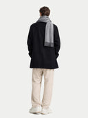 back view of a person wearing a black coat, gray scarf, and beige pants on a white background