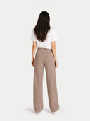 Back view of a woman wearing a white top and beige pants on a light gray background