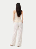 Woman wearing a beige sleeveless cashmere top and white pants on a white background. #color_off-white