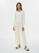 A woman modeling a matching off-white long-sleeve top and wide-leg cropped pants, paired with black slide sandals, against a plain white background. #color_white