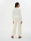 A woman modeling a matching off-white long-sleeve top and wide-leg cropped pants, paired with black slide sandals, against a plain white background. #color_white