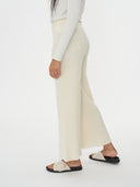 A woman modeling a matching off-white long-sleeve top and wide-leg cropped pants, paired with black slide sandals, against a plain white background. #color_white
