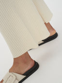 A woman modeling a matching off-white long-sleeve top and wide-leg cropped pants, paired with black slide sandals, against a plain white background. #color_white