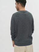 Man wearing a dark gray sweater and beige pants on a white background