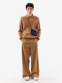 A man standing wearing a beige cashmere polo sweater with a round neckline and long sleeves. #color_light-brown